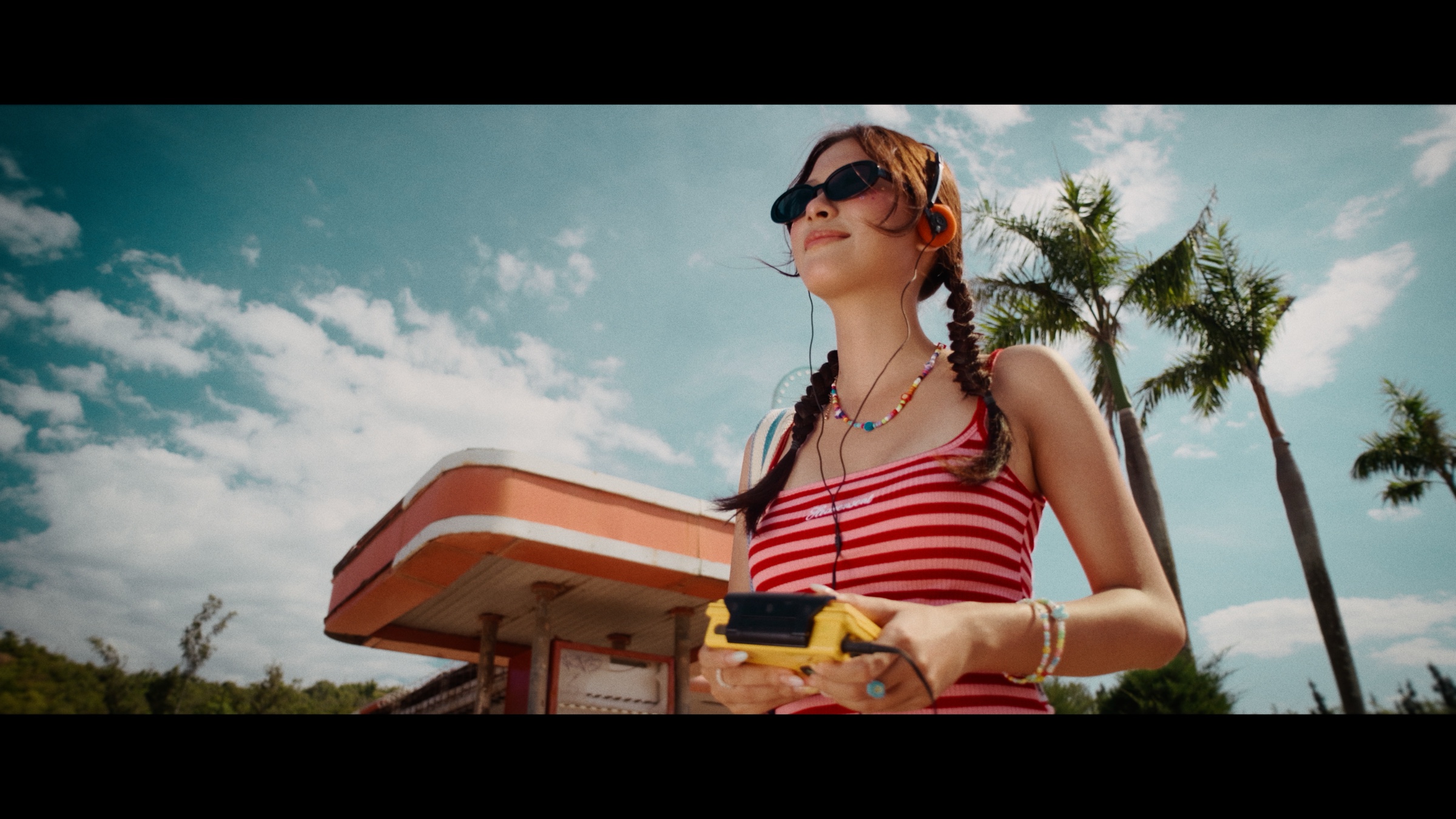Woman holding a camera beneath palms — after Coastal